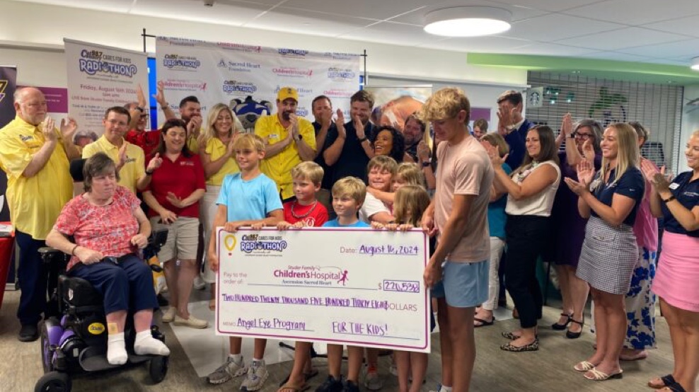 Photo of children holding a check with people in the background applauding